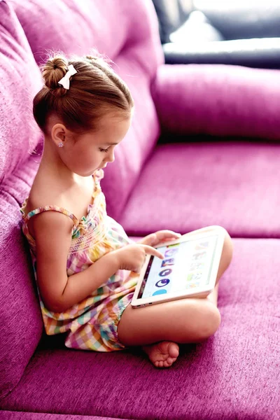 Маленькая симпатичная девочка с планшетным компьютером на диване дома — стоковое фото