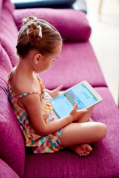 Маленькая симпатичная девочка с планшетным компьютером на диване дома — стоковое фото