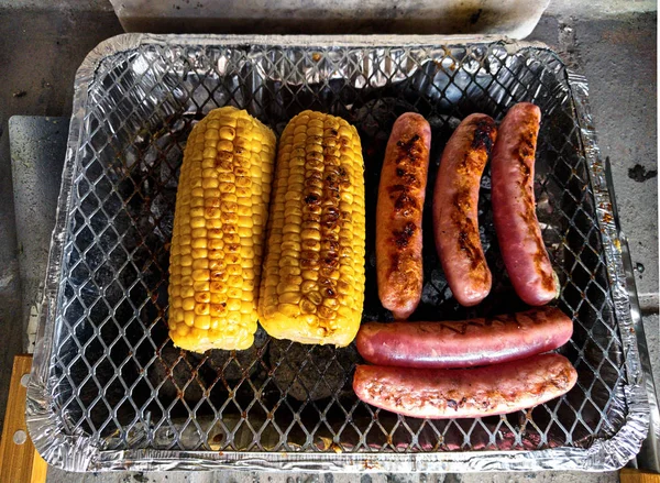 Sweet corn and sausages on the single use barbecue — Stock Photo, Image