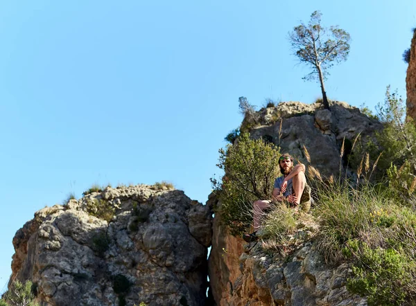 Bearded man traveler sitting on a mountain edge — Stock Photo, Image