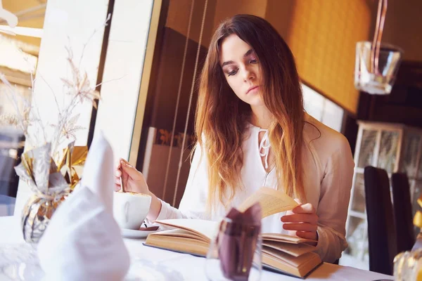 Mladá brunetka s knihou v restauraci — Stock fotografie