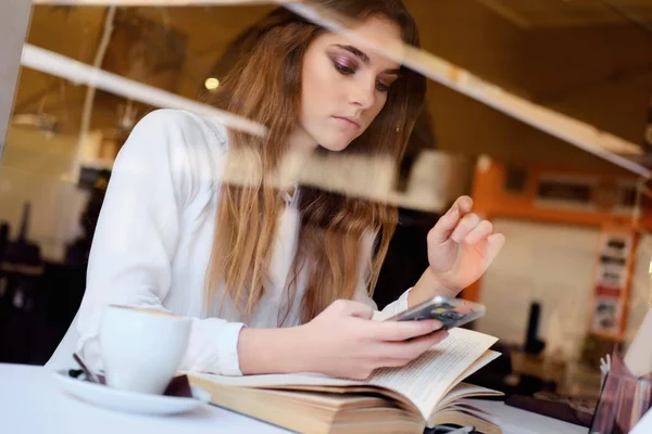 Ung brunett med en smartphone som sitter i en restaurang — Stockfoto