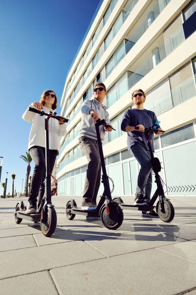 Three best friends young 20s -30s girl and guys spend time outdoors gathered together driving on electric scooter — Stock Photo, Image