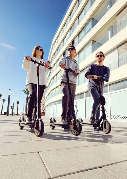 Três melhores amigos jovens de 20-30 anos menina e caras passar o tempo ao ar livre reunidos dirigindo em scooter elétrico — Fotografia de Stock