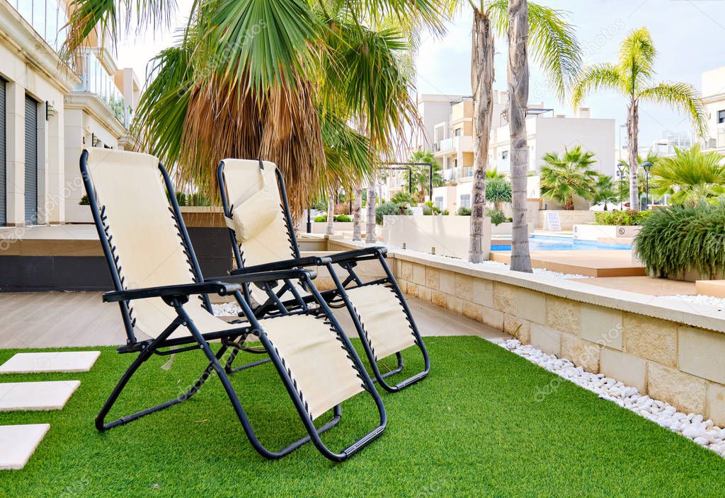 Two empty lounge chairs on artificial lawn grass inside of personal area backyard residential summer villa,