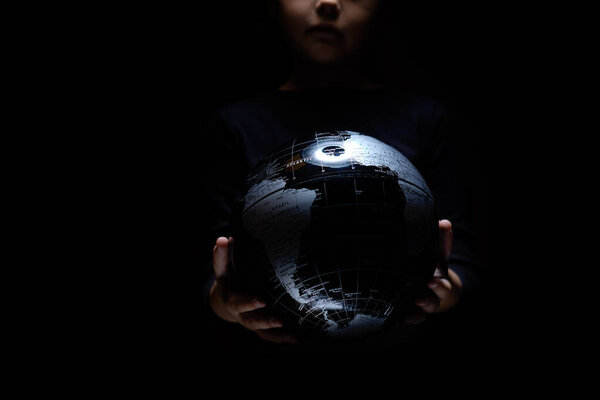 Руки маленькой девочки держащей карту шара глобуса изолированы на черном фоне. Пандемическая инфекция COVID-19. Загрязнение окружающей среды, экологическая катастрофа
