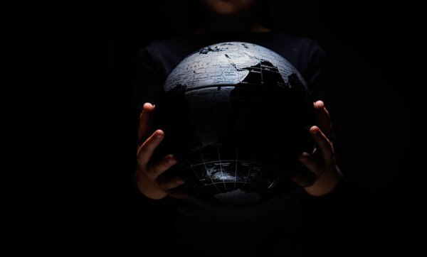 Руки маленького ребенка держат карту сферы земного шара изолированной на черном фоне. Пандемическая инфекция COVID-19. Загрязнение окружающей среды, экологическая катастрофа
