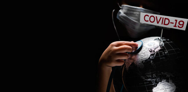Kid hold globe put stethoscope on sphere where shown sign COVID-19 red letters, face covered in mask on black background. Globally spread pandemic infection epidemic disease conceptual wide image