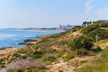 Dehesa de Campoamor yüksek katlı bir bina kasabası, Cabo Roig sahilinin kayalık sahili manzaralı. Sakin mavi Akdeniz, güneşli bir gün, insan yok. Orihuela, Torrevieja, Alicante, Costa Blanca, İspanya