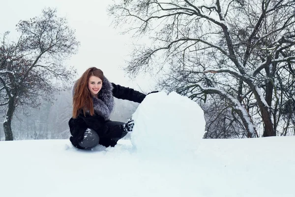 Uma mulher está rolando uma grande bola de neve — Fotografia de Stock