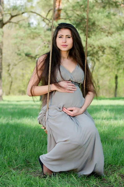 Mulher grávida no jardim em um balanço — Fotografia de Stock