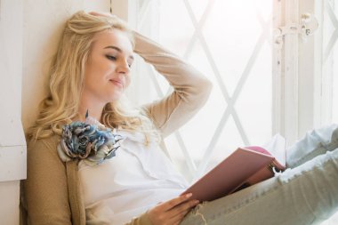 Çiçek şeklinde broşu olan genç bir kız kitap okuyor.