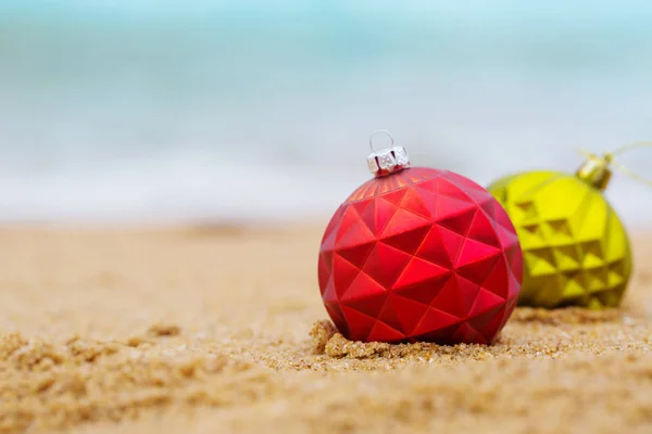 Rote und grüne Weihnachtskugel am Sandstrand — Stockfoto