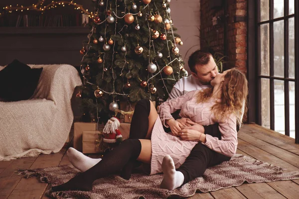 Loving couple kisses near the Christmas tree on the floor — Stock Photo, Image