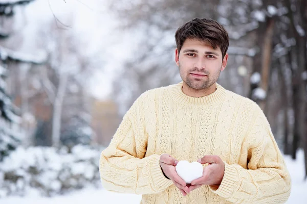 Snygg man med ett hjärta gjort av snö i händerna — Stockfoto