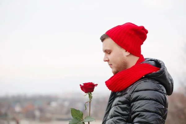 Um tipo pensativo com uma rosa vermelha, ao ar livre — Fotografia de Stock