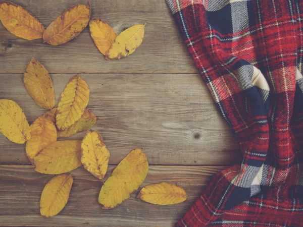 Flat lay view of autumn leaves and tartan textured scarf on wood — Stock fotografie