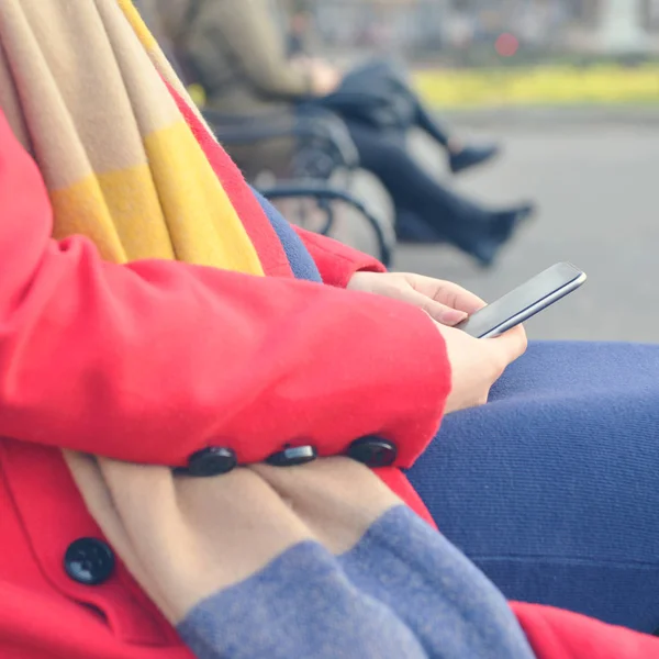 Kobieta za pomocą telefonu komórkowego, siedząc na ławce w parku na zewnątrz — Zdjęcie stockowe
