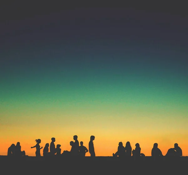 Grupp av unga människor som sitter på väggen vid solnedgången — Stockfoto