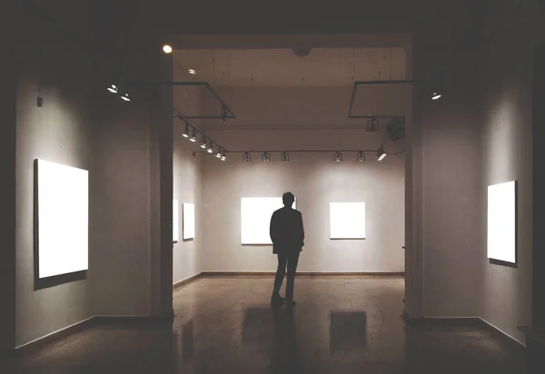 Hombre en la sala de la galería mirando marcos de imágenes vacías - Mock up ar —  Fotos de Stock
