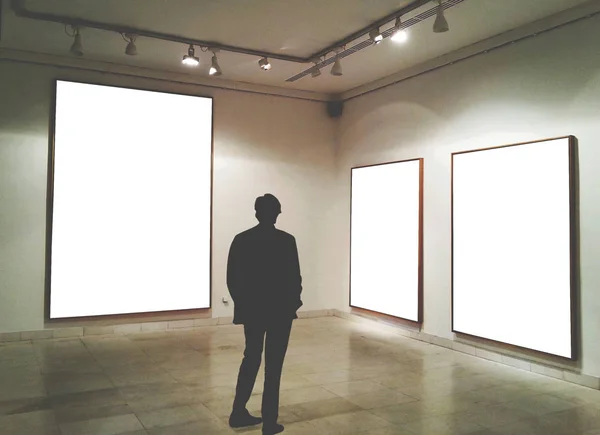 Man in gallery room looking at empty picture frames - Mock up ar — Stock Photo, Image