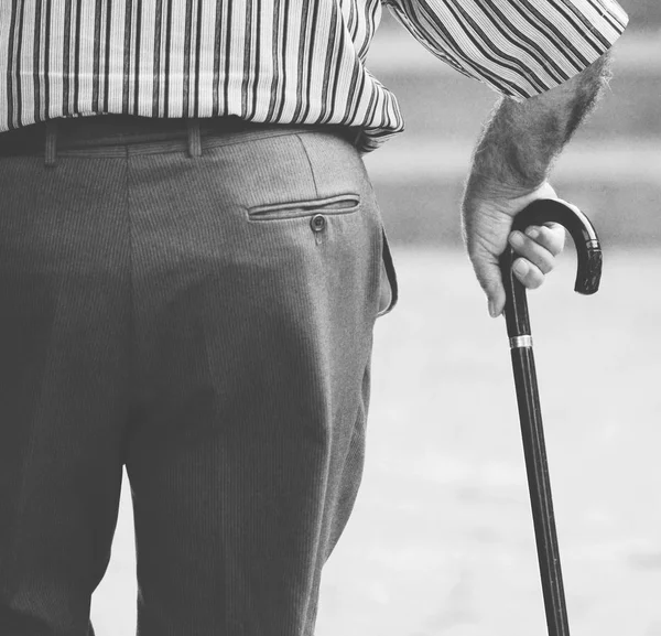 Old man walking with his hands on a wooden walking stick — Stock Photo, Image