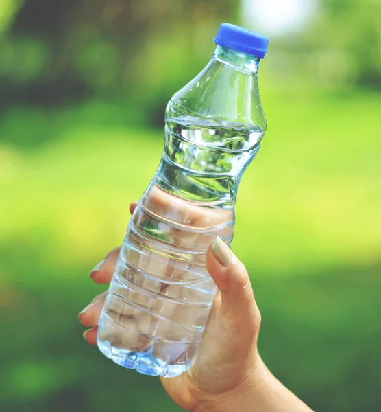 Vrouw hand houden water fles tegen groene achtergrond — Stockfoto