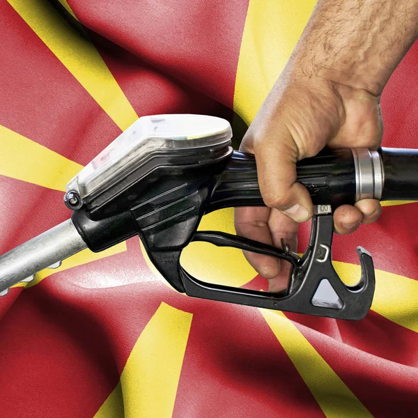 Gasoline consumption concept - Hand holding hose against flag of