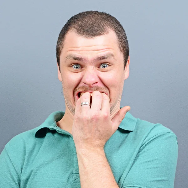 Portrait of a man biting nails and being scared against gray bac — Stock Photo, Image