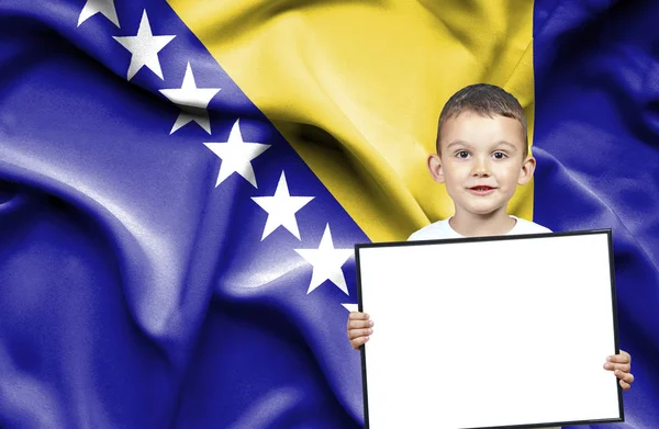 Lindo niño pequeño sosteniendo el cartel de emtpy delante de la bandera de Bosnia y —  Fotos de Stock
