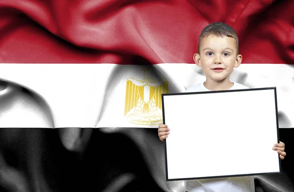 Симпатичный маленький мальчик с эмпатичным знаком перед флагом Египта — стоковое фото