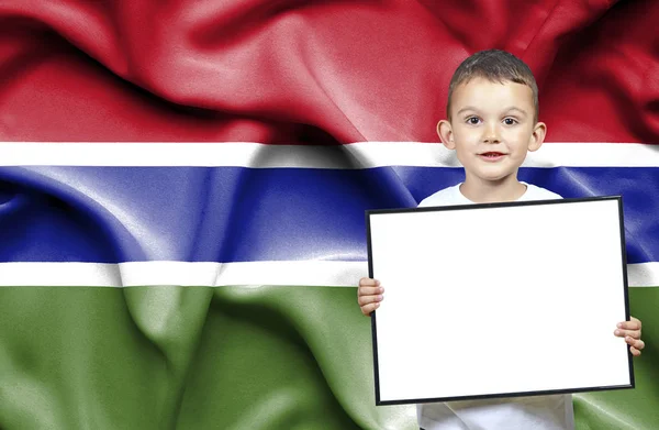 Lindo niño pequeño sosteniendo el cartel de emtpy frente a la bandera de Gambia — Foto de Stock