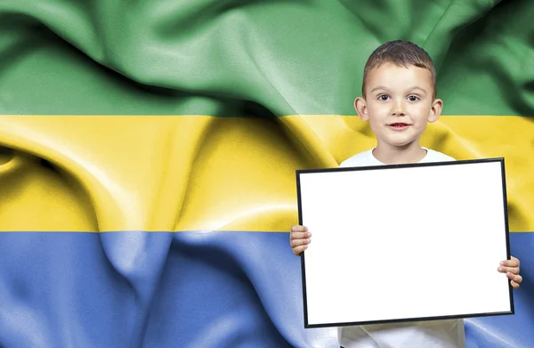 Cute small boy holding emtpy sign in front of flag of Gabon — Stock Photo, Image