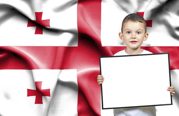 Carino piccolo ragazzo che tiene segno emtpy davanti alla bandiera della Georgia — Foto Stock