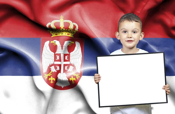 Bonito menino pequeno segurando sinal emtpy na frente da bandeira da Sérvia — Fotografia de Stock