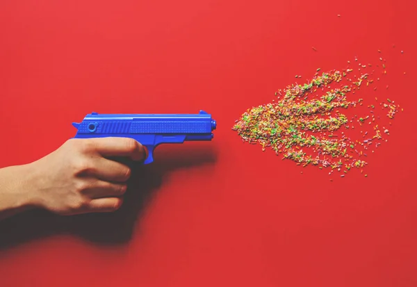 Mão segurando pistola e disparando doces multicoloridos - Flat lay — Fotografia de Stock