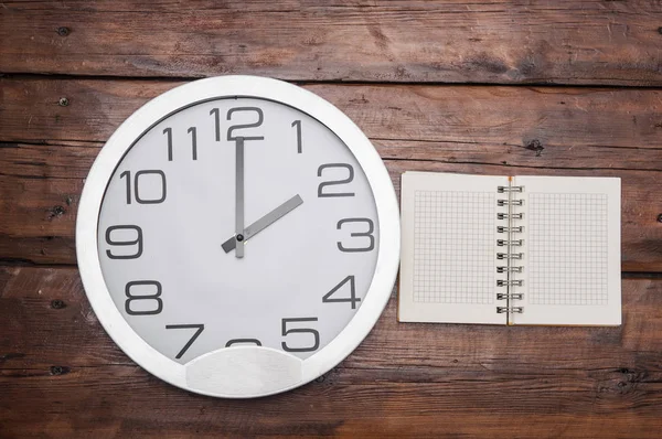 Blank notebook with wall clock on wood table. — Stock Photo, Image