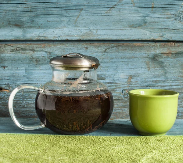 Průhledná skleněná čajník s černého čaje a barevné šálky na dřevěný stůl — Stock fotografie