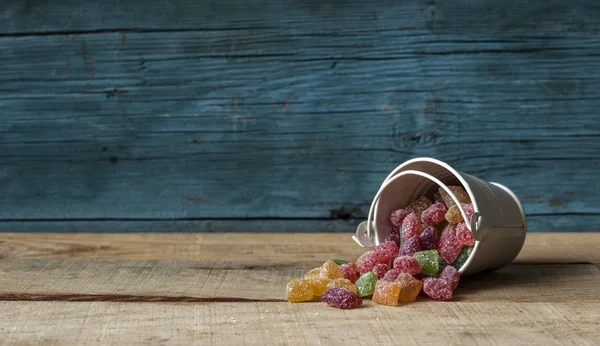 Bunte Bonbons und blauer Eimer auf Holz Hintergrund — Stockfoto