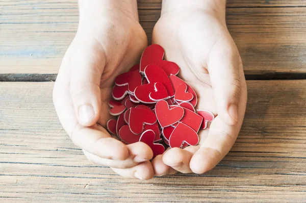 Rode harten in handen close-up op houten achtergrond — Stockfoto