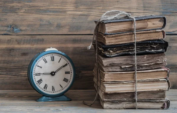 Vecchio orologio su un vecchio tavolo di legno con una pila di libri — Foto Stock