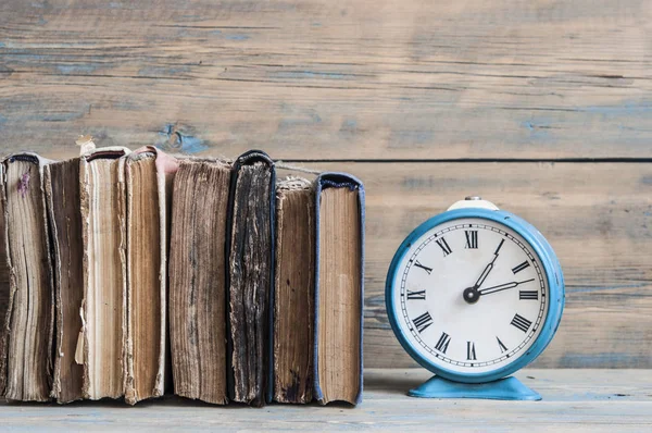 Eski bir kitap yığını ile eski bir ahşap masa saati