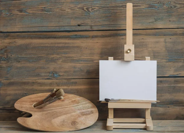 Paleta de cavalete aquarelas e pincéis com tela branca vazia — Fotografia de Stock