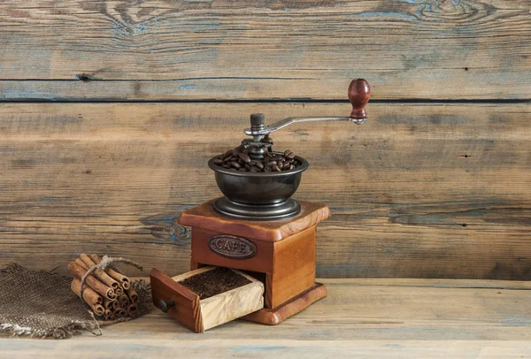 Zátiší s kávová zrna a starý mlýnek na dřevěný stůl — Stock fotografie