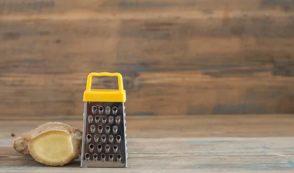 Çelik rende ve ahşap masa üzerinde zencefil kökü — Stok fotoğraf