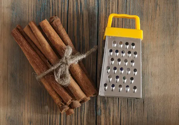 Palitos de canela y rallador de acero sobre fondo de madera — Foto de Stock