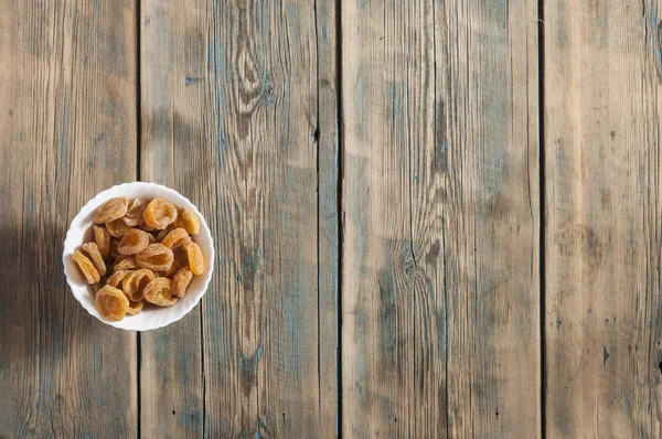 Dried apricots in the bowl on the wood background, top view — Stock Photo, Image