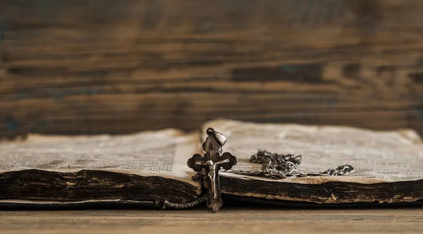 La religion. Une croix avec une chaîne contre un vieux livre — Photo