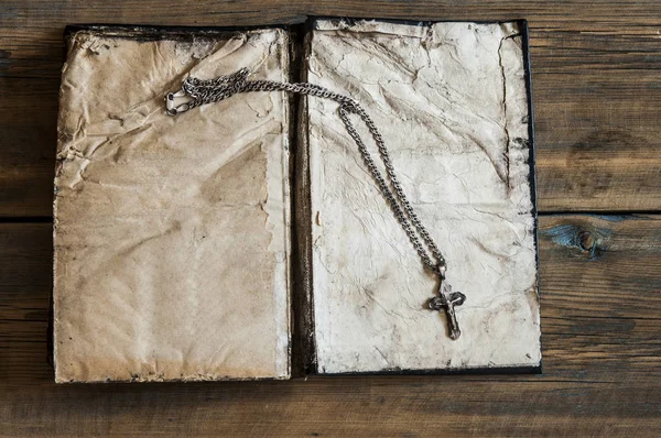 Religie. een kruis met een keten tegen een oud boek — Stockfoto