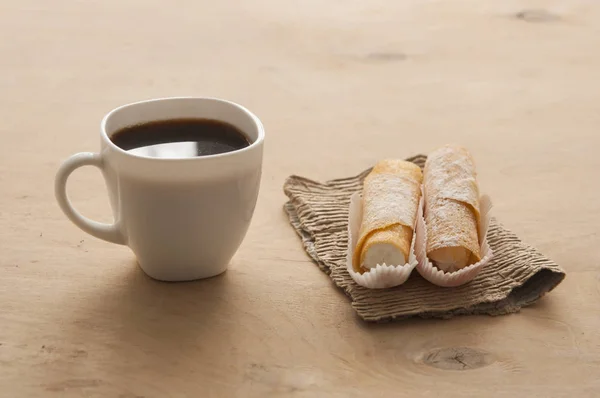 Сладкая закуска с кофе и вафельными трубками на деревянном фоне — стоковое фото